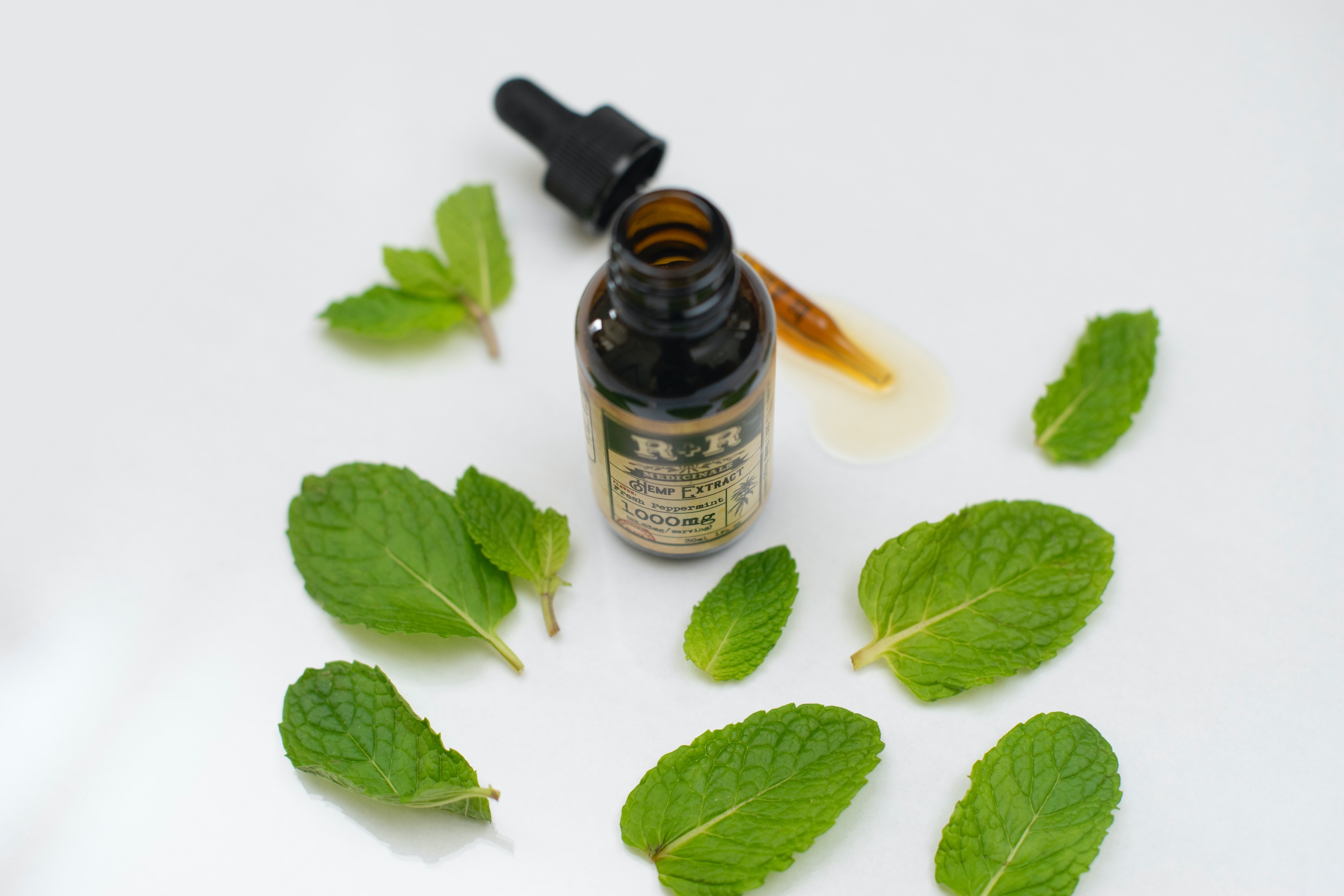 A small brown bottle and dropper are surrounded by green peppermint leaves.