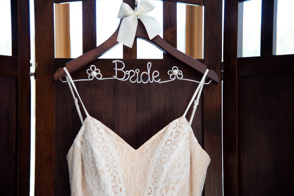 A wedding dress hangs on a hanger with the word "bride" spelled out in wire.