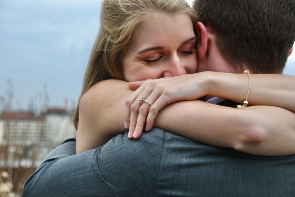 A woman with an engagement ring on hugs a man.