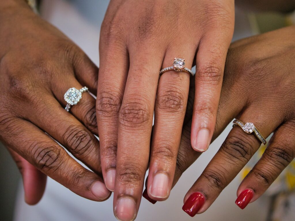 Three hands display three different engagement rings.