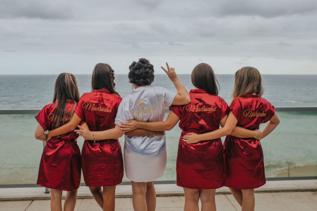 Four bridesmaids wearing red silk robes stand around a bride in a white silk robe. 