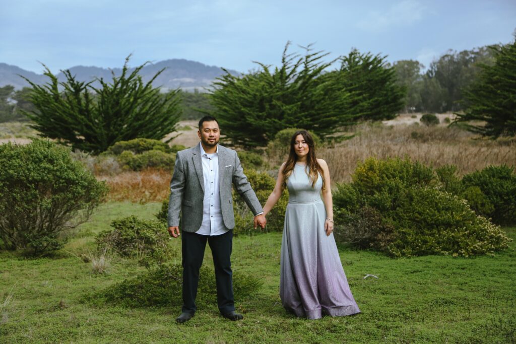 A man in a grey suit and a women in a purple ombre dress hold hands