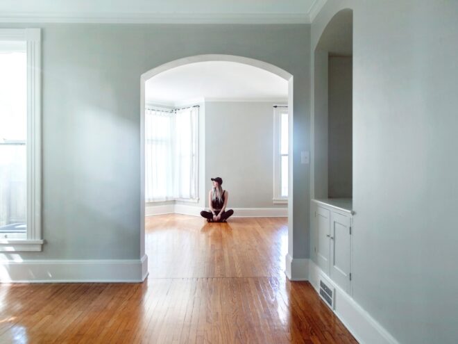 A woman sits on the floor in an empty house.