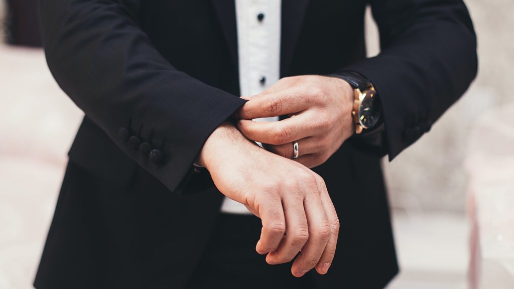 A close up photo of a man in a black tuxedo with a wedding ring. 