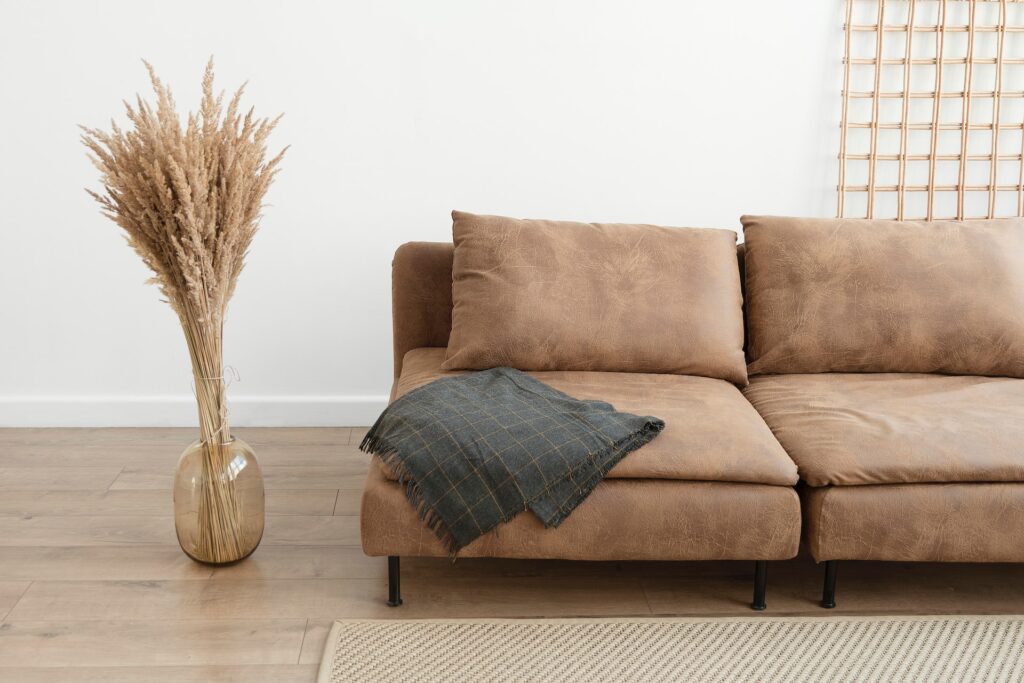 A simple brown couch sits next to a vase of pampas grass.