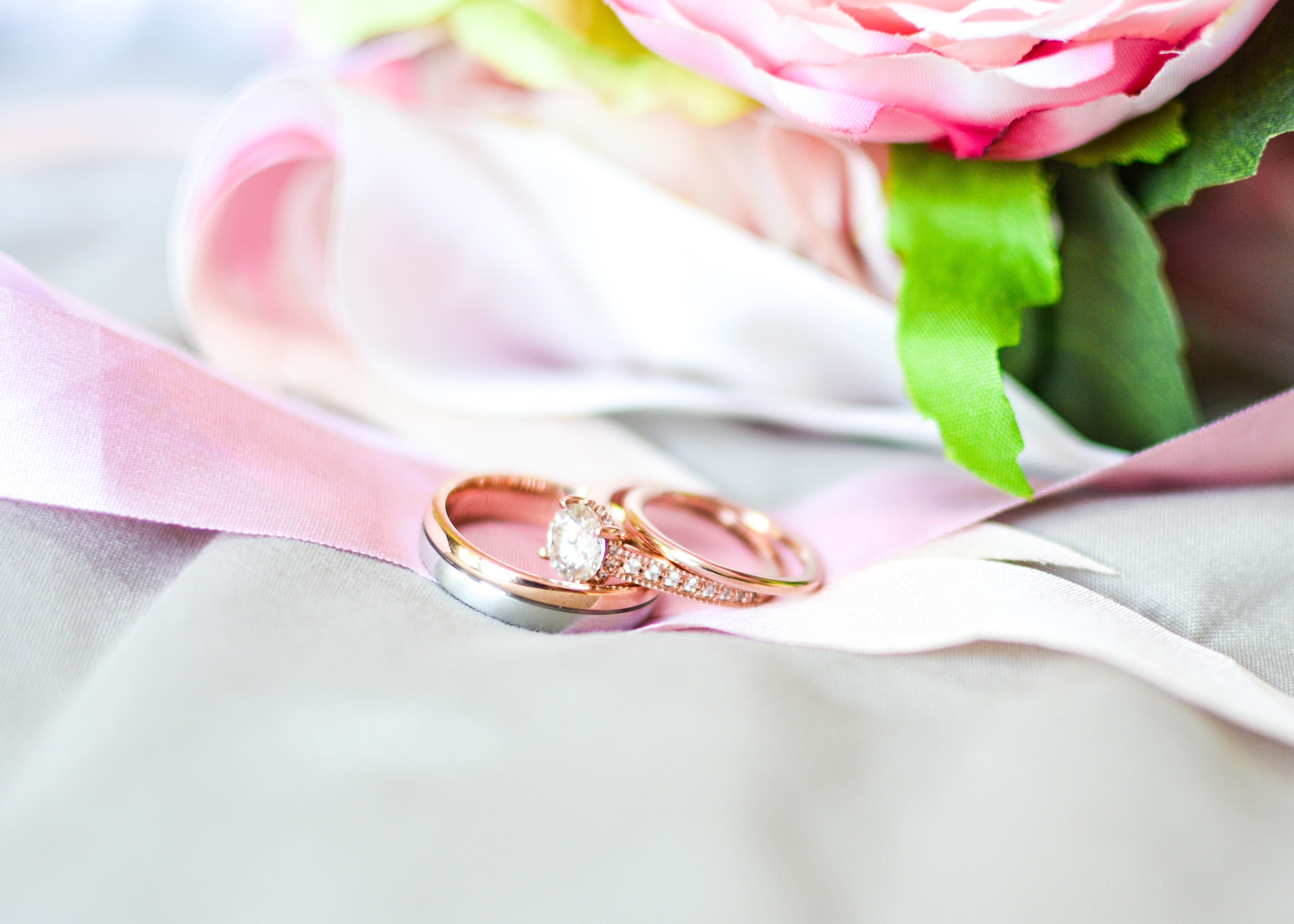 An engagement ring and wedding band sit on a pink ribbon.