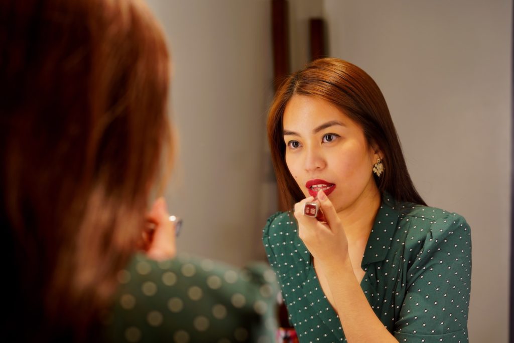 A woman applies red lipstick.
