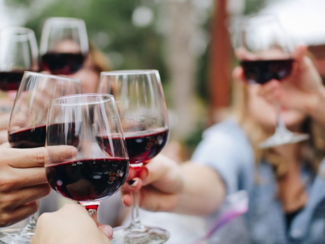 a group of friends clinking wine glasses who need to know how to get red wine out of clothes