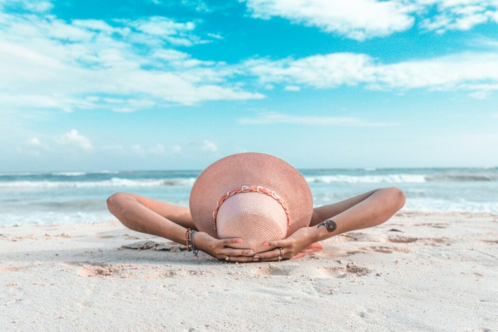 A woman wearing a straw hat lays on the beach. 