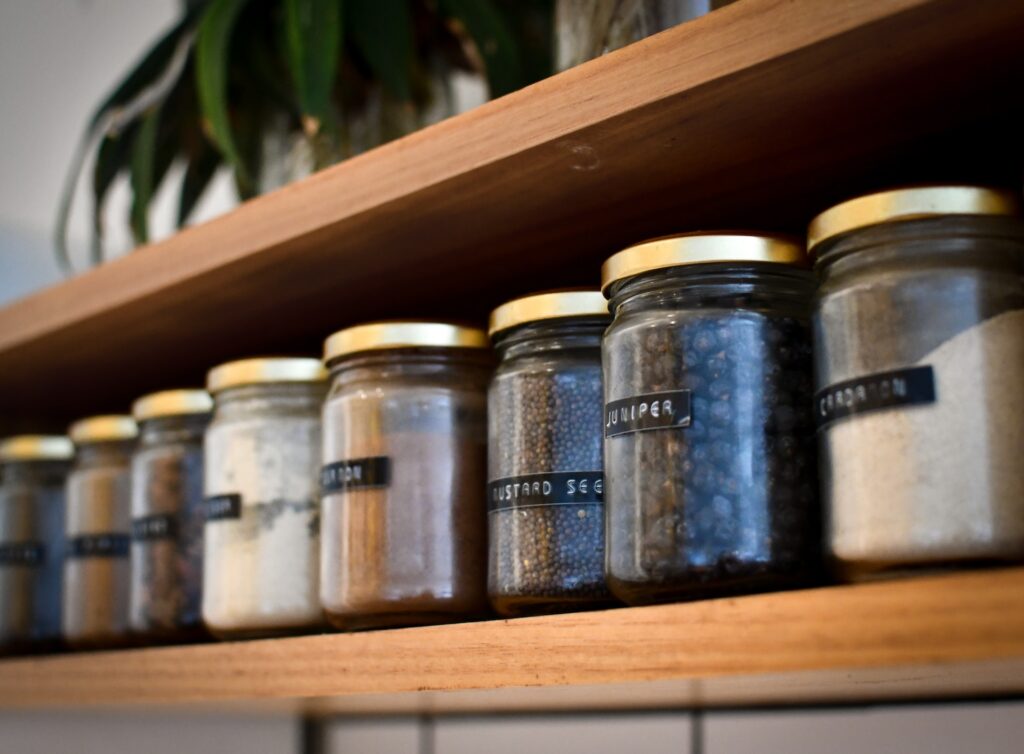 Glass jars with kitchen ingredients in them sit on a pantry shelf.