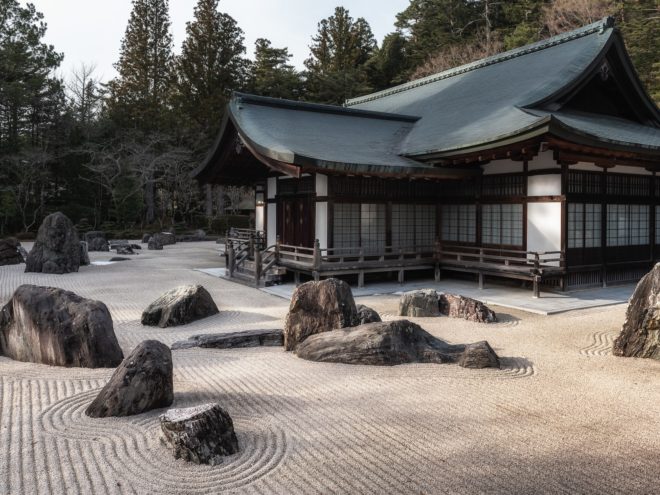 A meditation garden with rocks and sand surrounds a Japanese-style house.