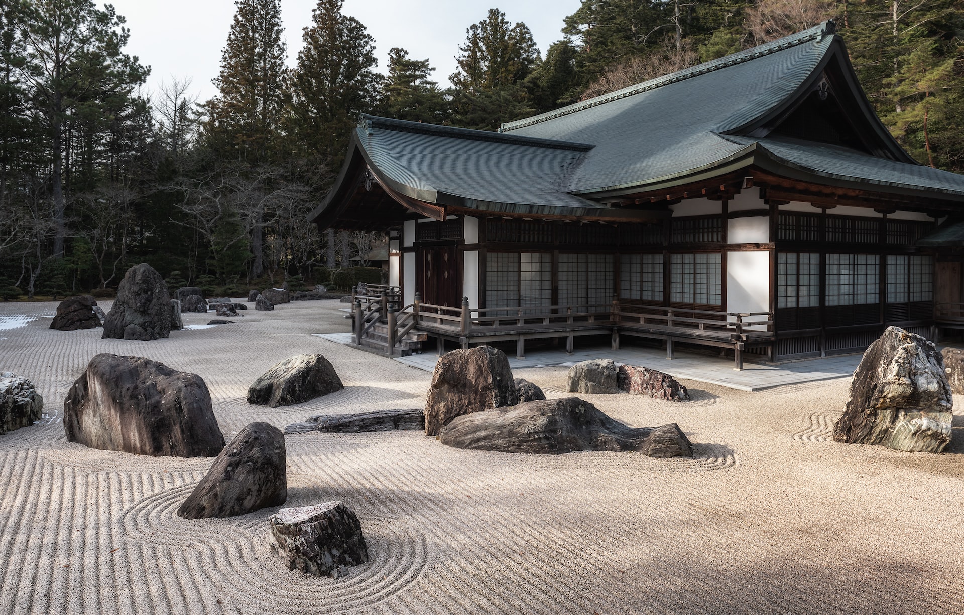 A meditation garden with rocks and sand surrounds a Japanese-style house.