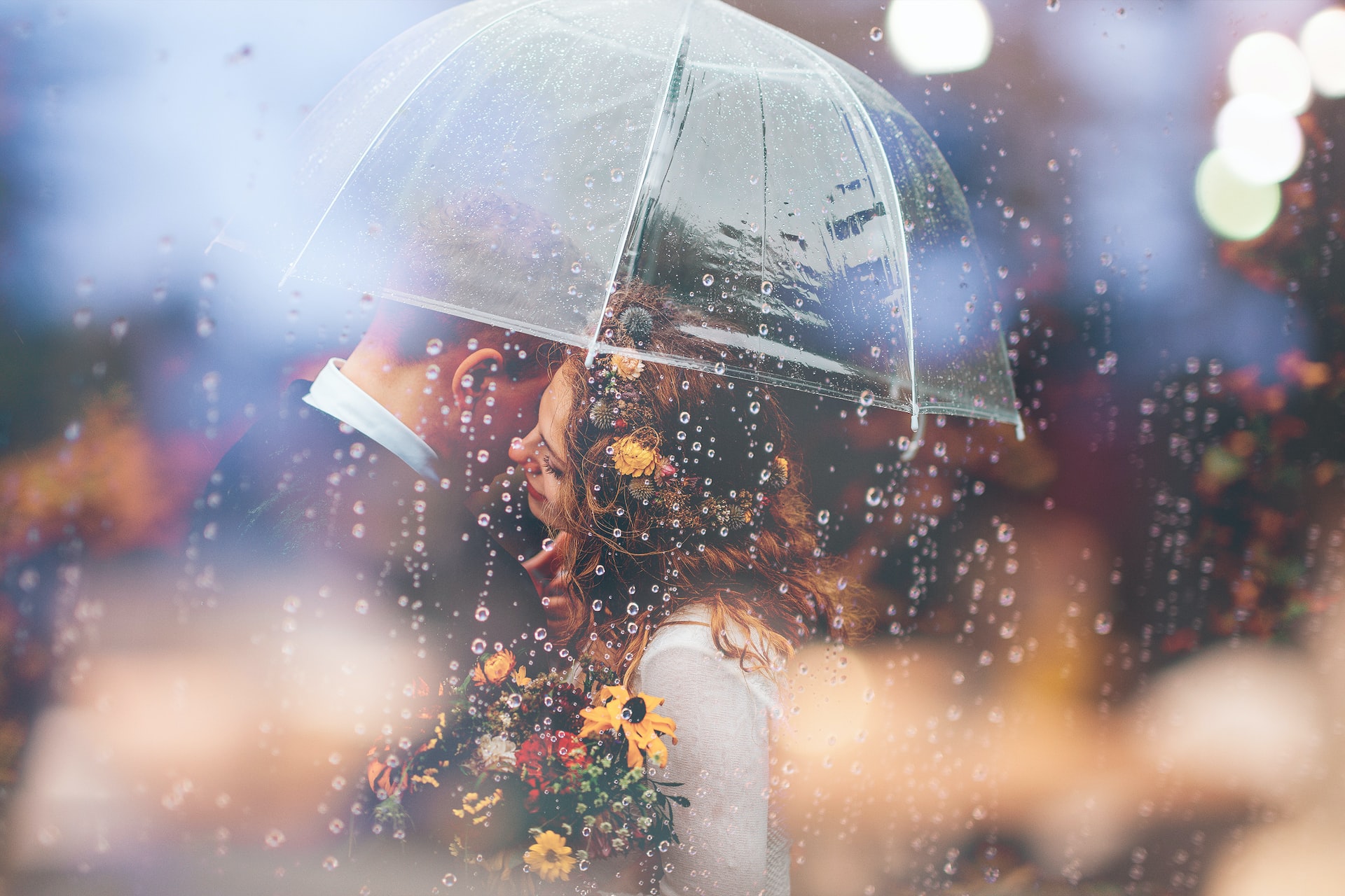 A bride and groom stand under an umbrella in the rain.