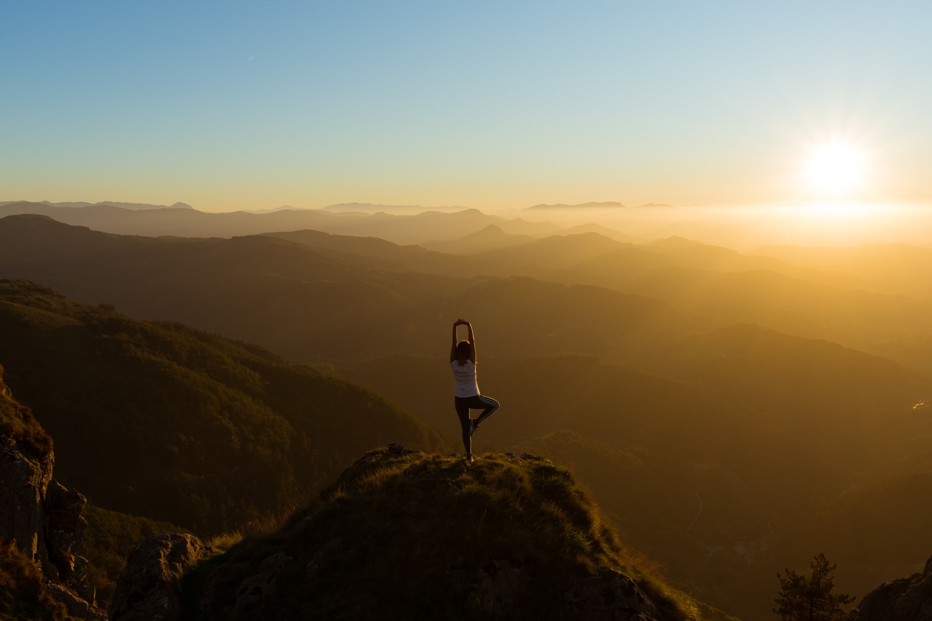 A person practicing yoga on a cliff at sunrise.