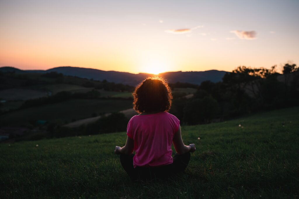 A woman meditates outside overlooking the sunset. 