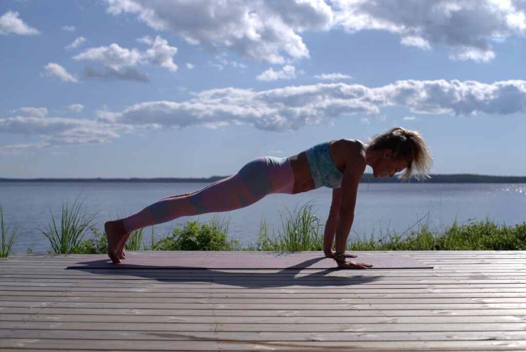 A woman does a plank overlooking a body of water. 