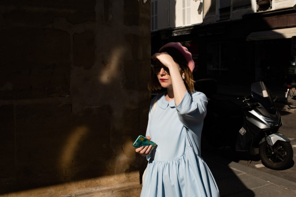 A woman in a blue dress and a pink beret shields her eyes from the sun.