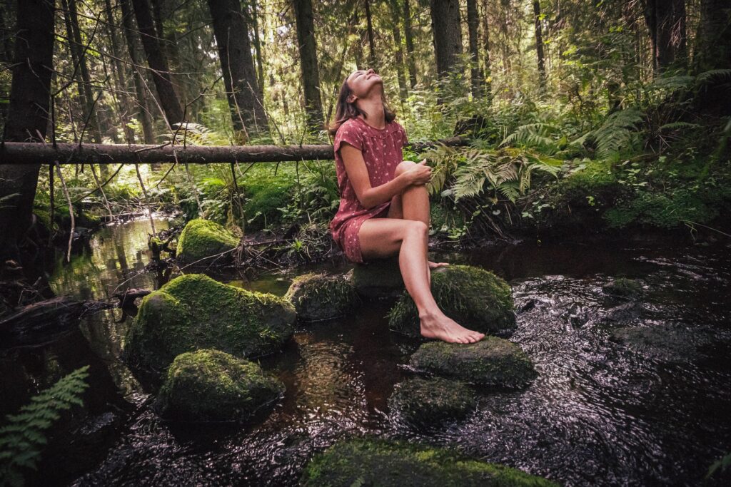 A woman sits on a rock in the forest. 