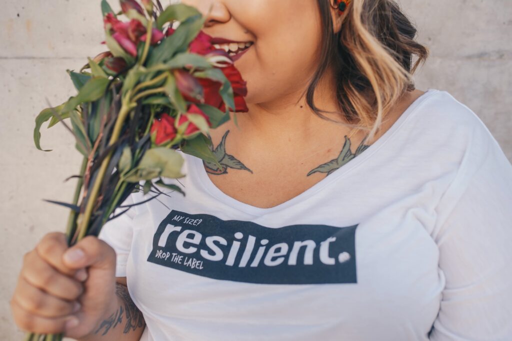 A woman holding flowers and wearing a shirt that says resilient.