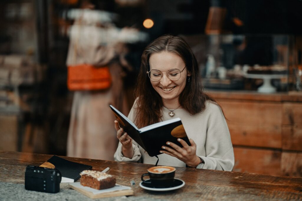 A woman sits in a cafe with a journal open in her hands.