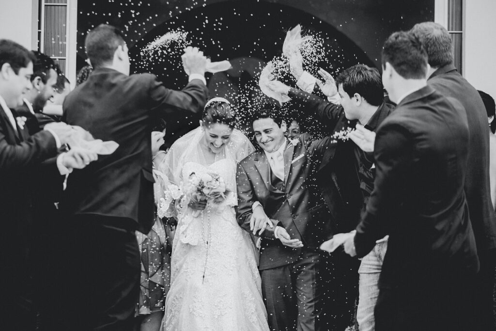 A bride and groom exit a church as guests throw rice.