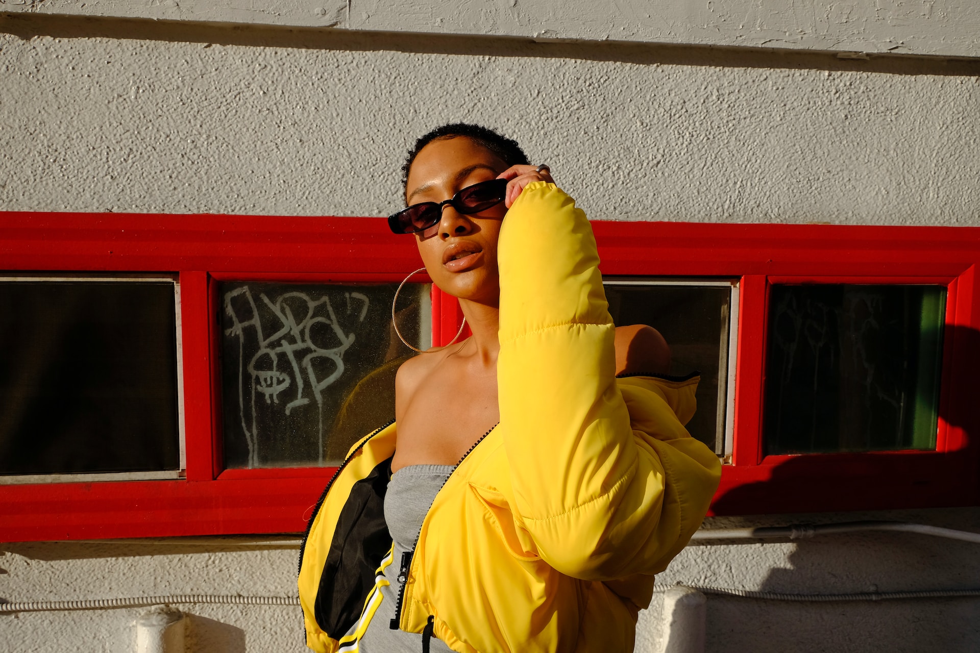 A woman wearing a yellow puffer jacket, sunglasses and hoop earrings.