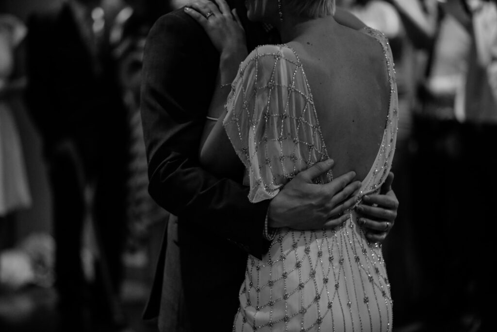 A woman wearing a vintage beaded wedding dress dances with a man in a suit. 