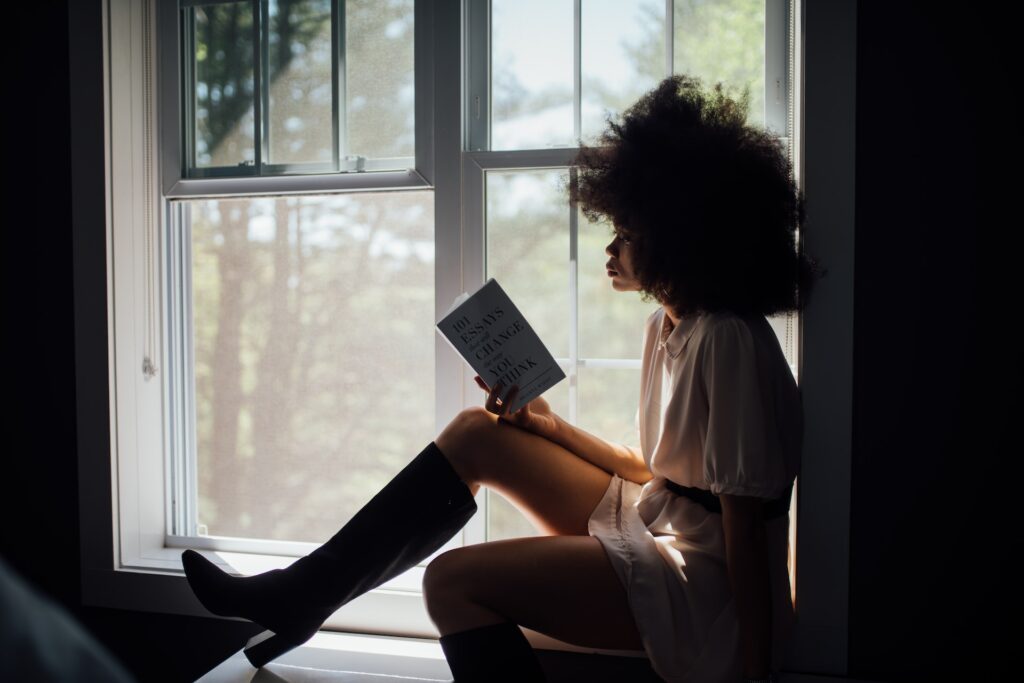 A woman sitting on a window sill reading.