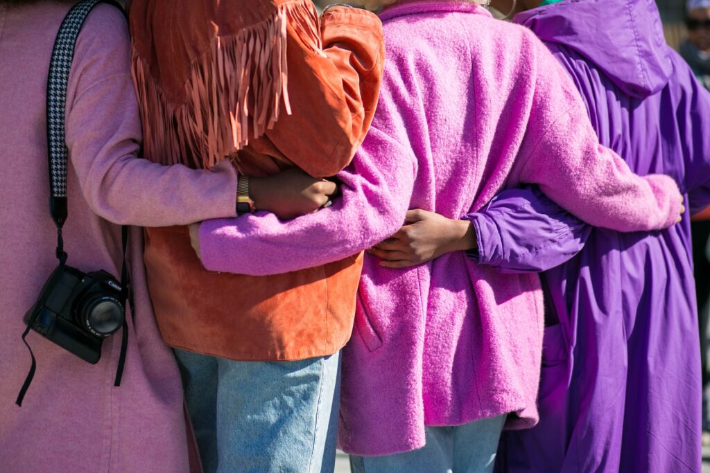 Women wearing bright colored clothing stand with their arms around each other.