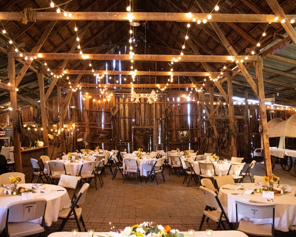 A barn set up for a wedding reception, with tables, chairs and string lights.
