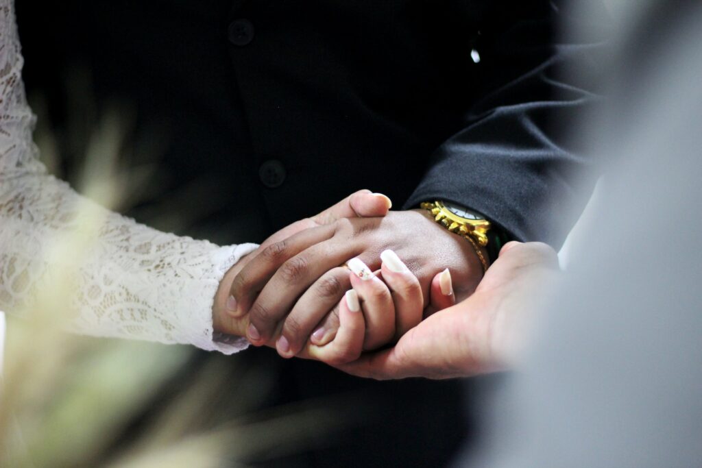 A couple holds hands with a wedding officiant's hand resting below.