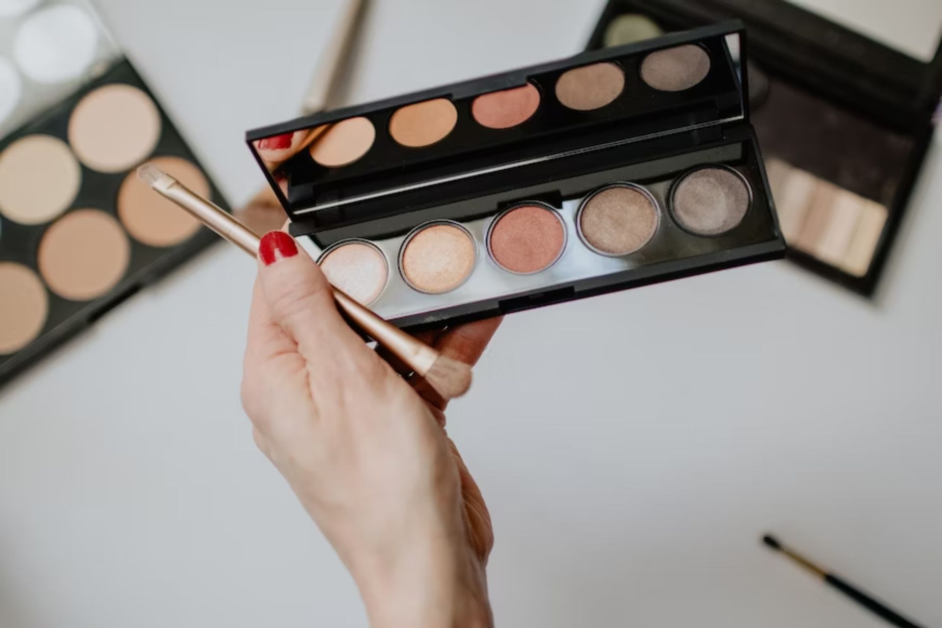 A person holds a neutral-colored eyeshadow palette with five colors. They range from light to dark. Learning how to do natural makeup involves learning which colors work best to leave you looking like you have little makeup on at all.