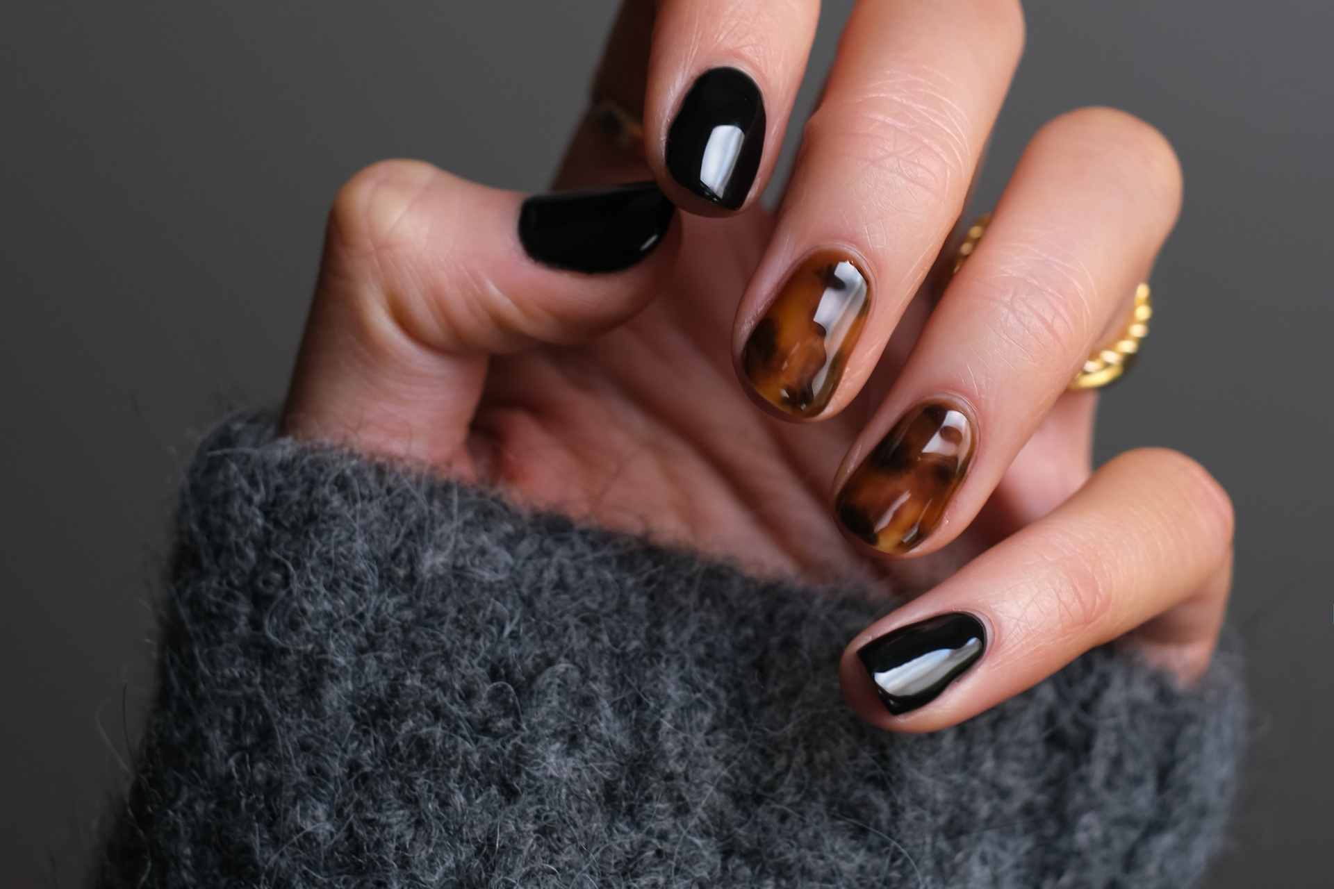 A woman's hand curled into a slight first to display her gel polish manicure where there nails a painted black and two have a tortoise shell print