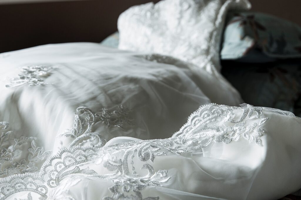 A white, lacy wedding dress is draped on top of pillows.