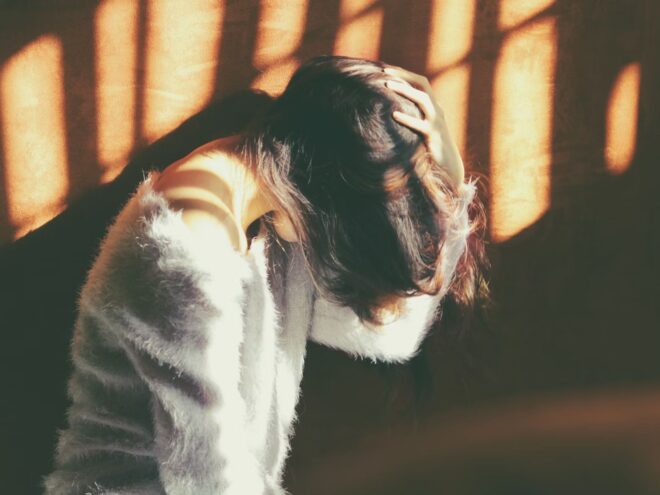 The picture depicts a woman holding her head, brown hair covering her face, blocking out the sunlight. In learning how to use essential oil for headaches, you may not need to experience this same pain as often or intensely.