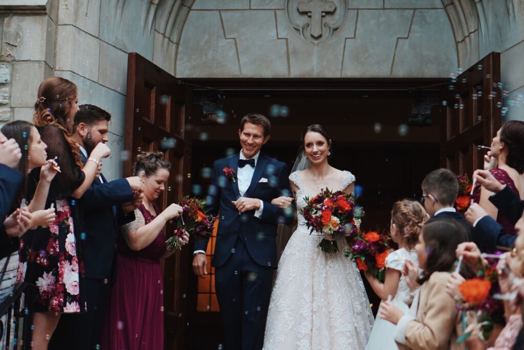 A bride and groom exit a church surrounded by guests.