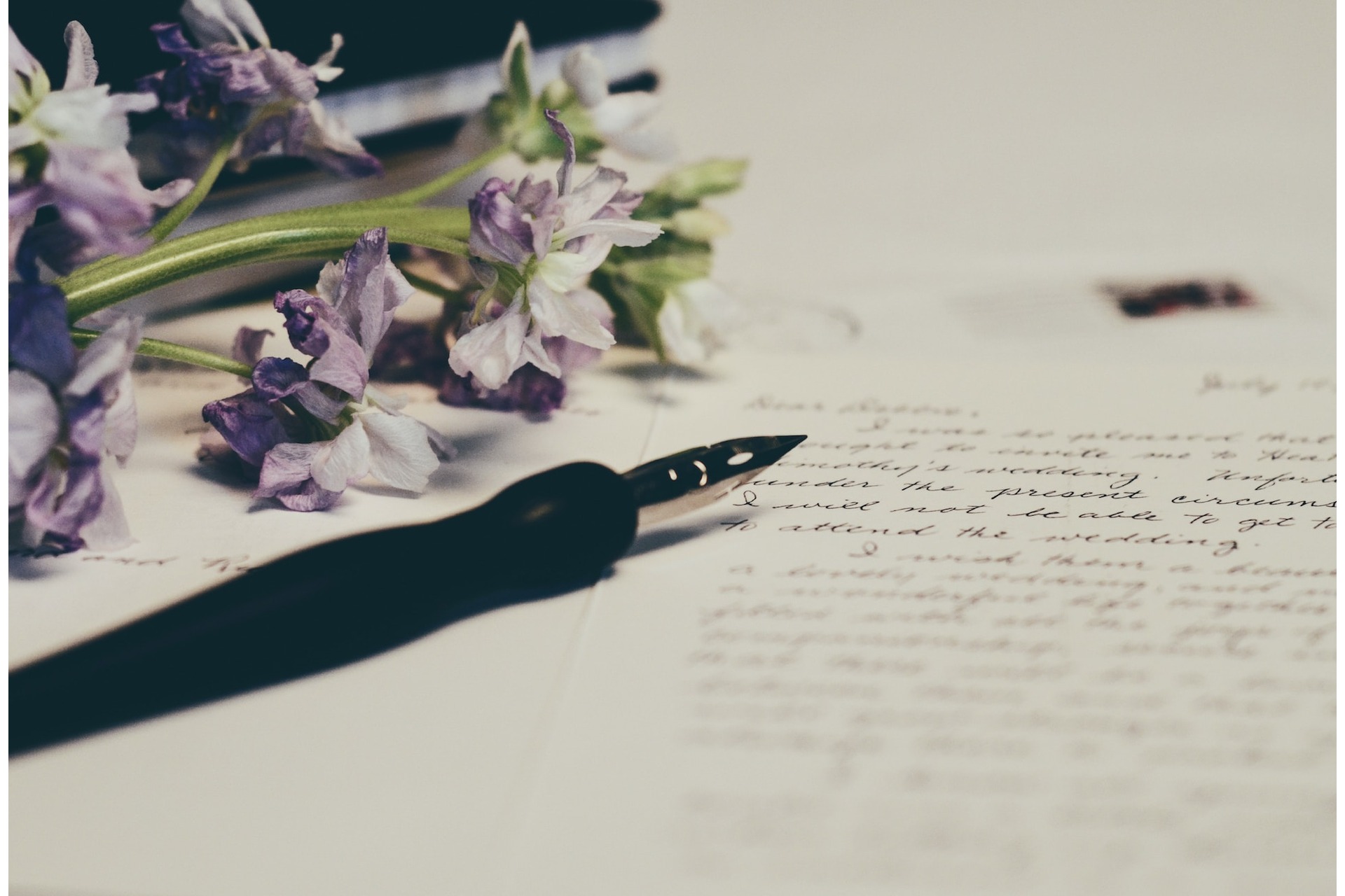 A pen and a wedding message to a couple with cursive writing, accompanied by purple flowers