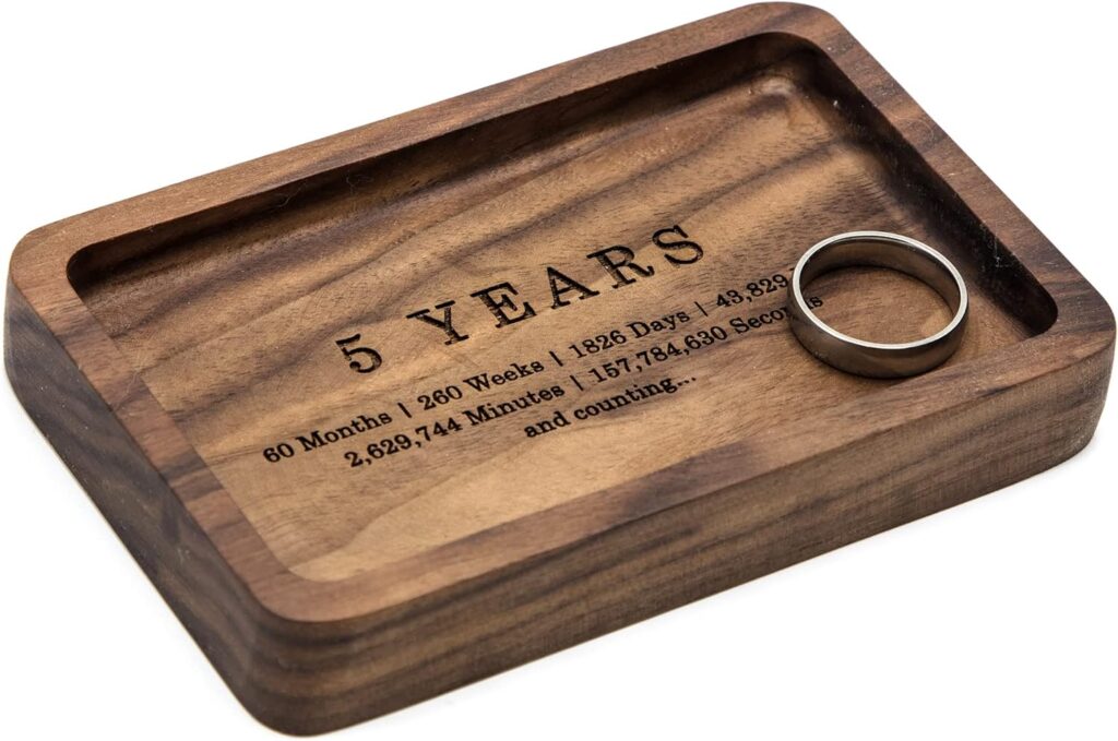 A dark wooden ring dish with 5 Years holds one silver wedding band against a white background.