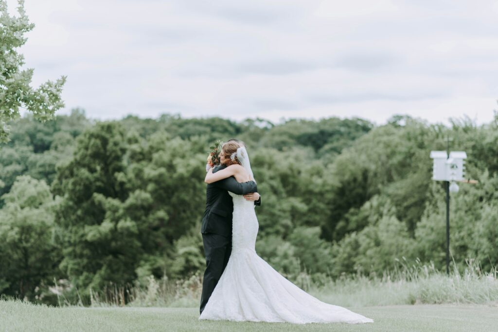 A bride hugs her father at an outdoor wedding. 