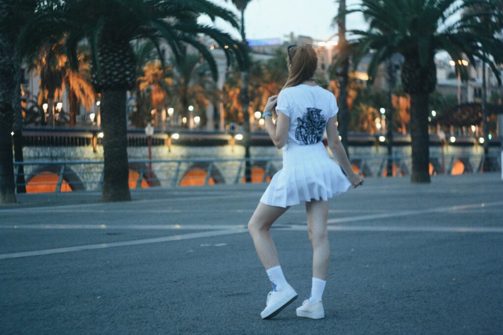 A woman wearing a white pleated skirt, calf-length socks and white sneakers.