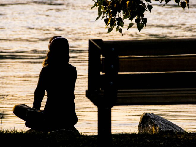 A woman sits and meditates by a river.