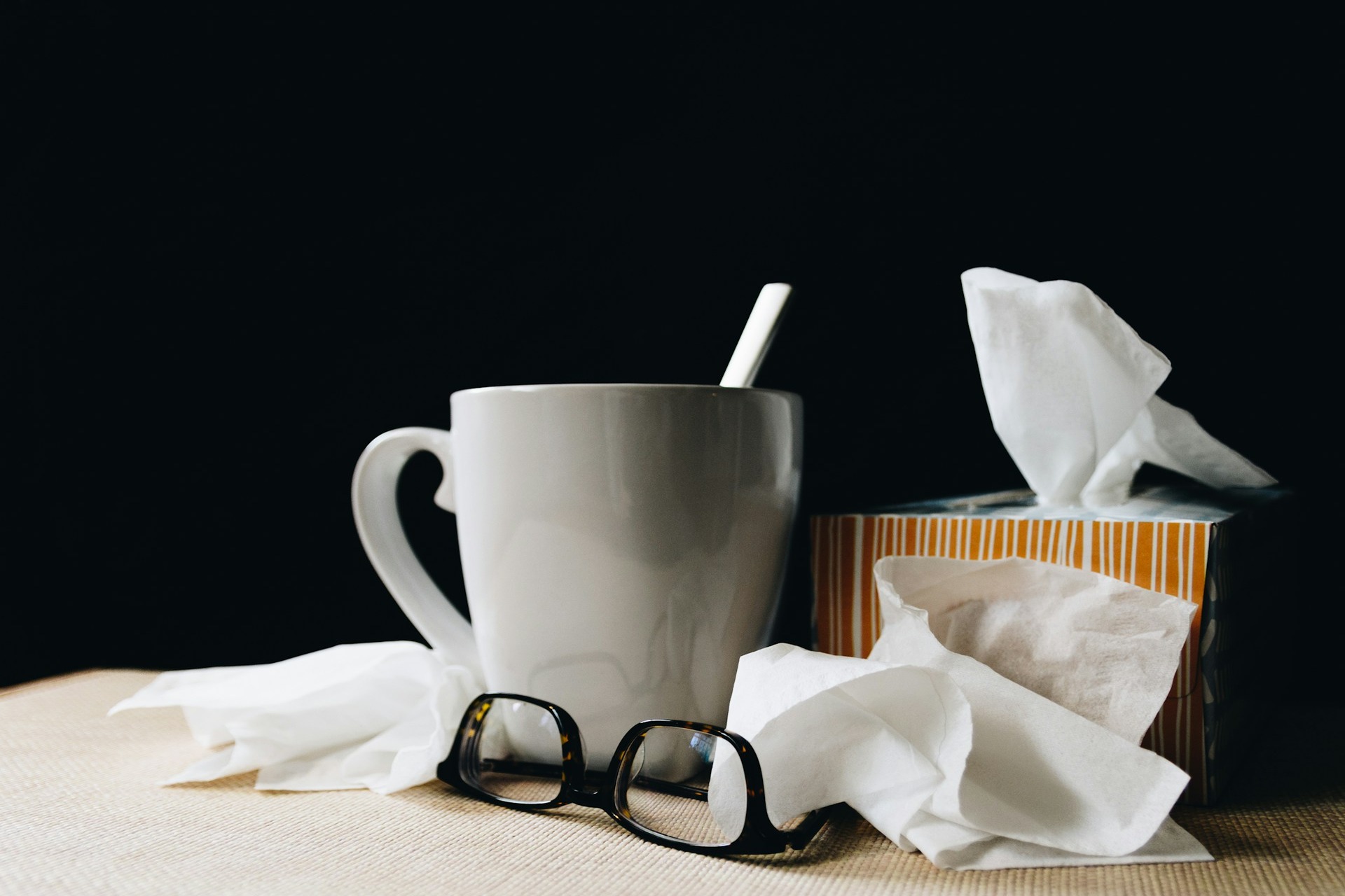 White cup with tissues and a pair of glasses.