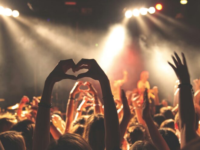 Person holding up a heart sign in a crowd of people.