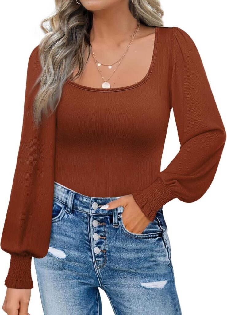 A woman stands in ripped jeans, a gold layered necklace and a long sleeved shirt with a square neck. It's an autumn brown color and has billowing sleeves.