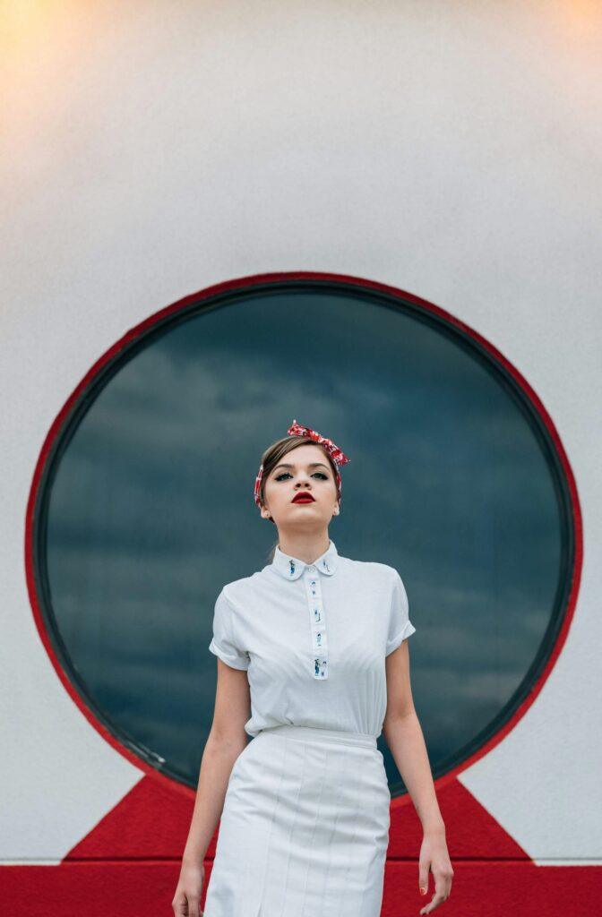 A woman wearing a blue collared dress, a red bandana and red lipstick.