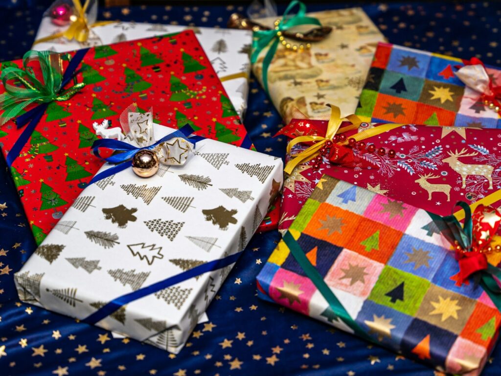 Seven rectangular presents in multi-colored and mismatched wrapping paper sit on a blue table cloth covered in gold stars. They're perfect for anyone who loves a colorful Christmas aesthetic.