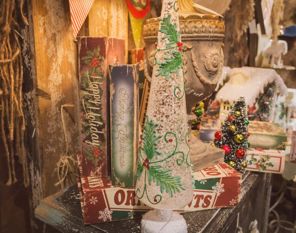 Thrifted wooden Christmas decor like planters and fake books sit among mini trees on a rustic dark wood dresser. It all encapsulates a vintage Christmas aesthetic.