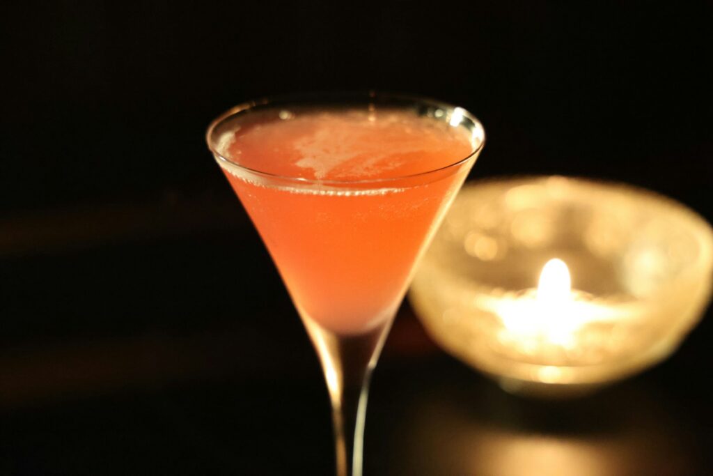 A pumpkin martini sits against a white background and a candle