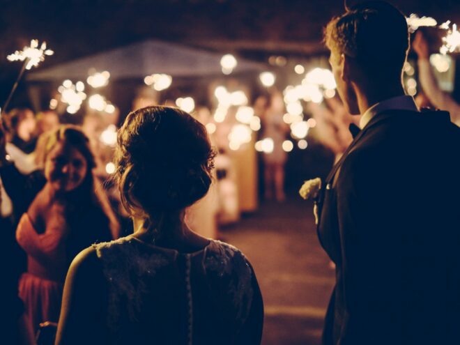 Type of holiday weddings with a man standing near a woman during nighttime.