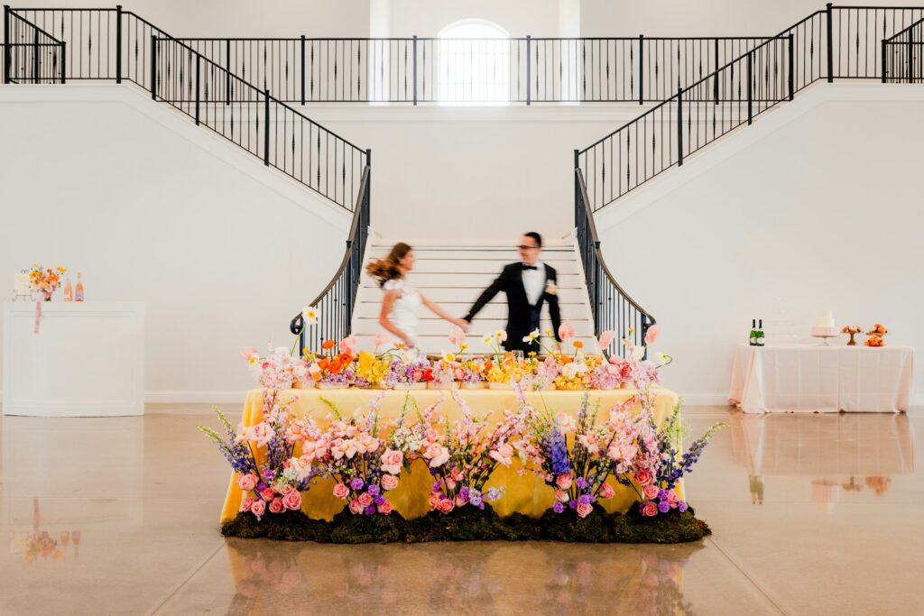 A bride and groom walk behind an arrangement of bright, neon florals. 